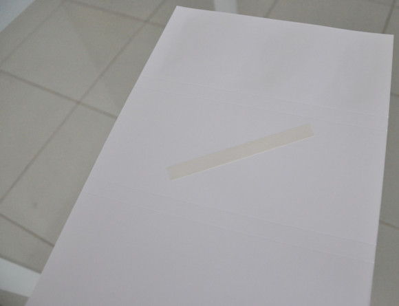 Cole uma tira de fita dupla face no centro do papel, pelo lado avesso