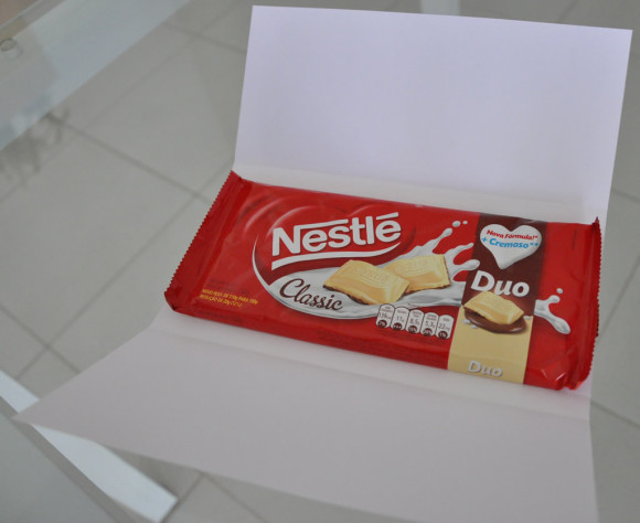 Retire a fita protetora e cole a barra de chocolate centralizada sobre a fita dupla face